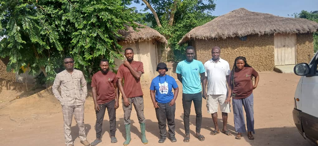 Group photograph of the visit team standing outdoors near thatched-roof buildings