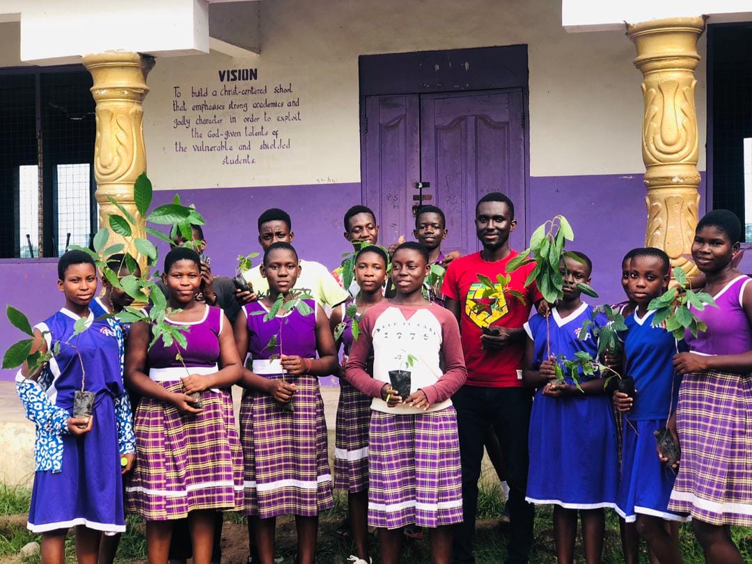 Students in school uniform holding seedlings in front of a school building, image 12 of 12