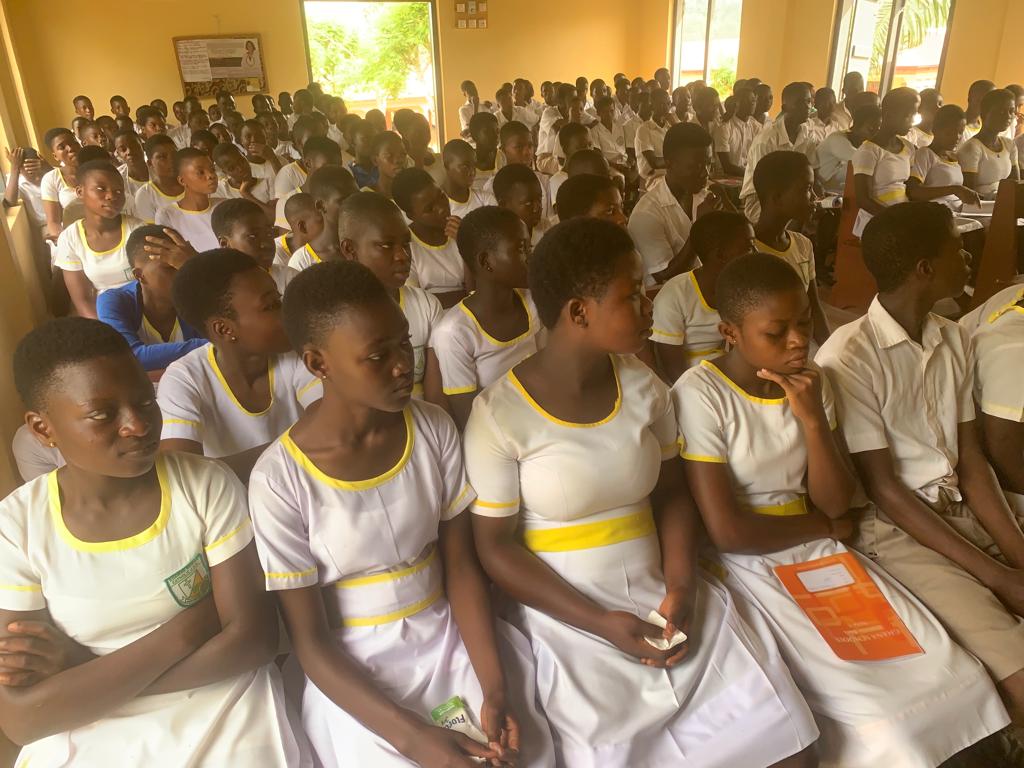 Rows of students in white school uniform seated together indoors, image 11 of 12
