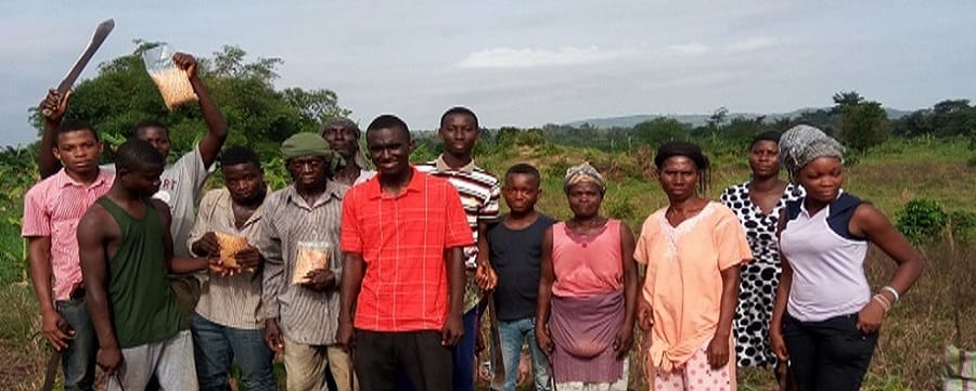 A group of men and women standing in a line outdoors, some holding tools and small packets, image 1 of 5
