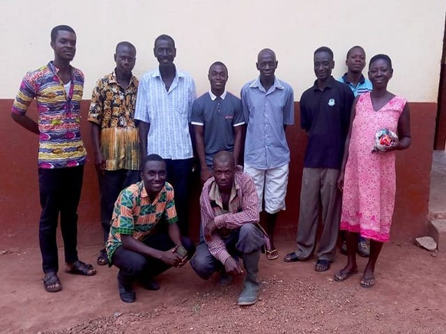 A group of men and a woman posing in front of a building wall, image 2 of 5