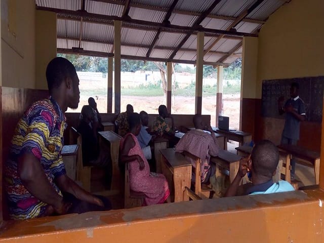 Participants seated on benches in an open-sided classroom during a session, image 3 of 5